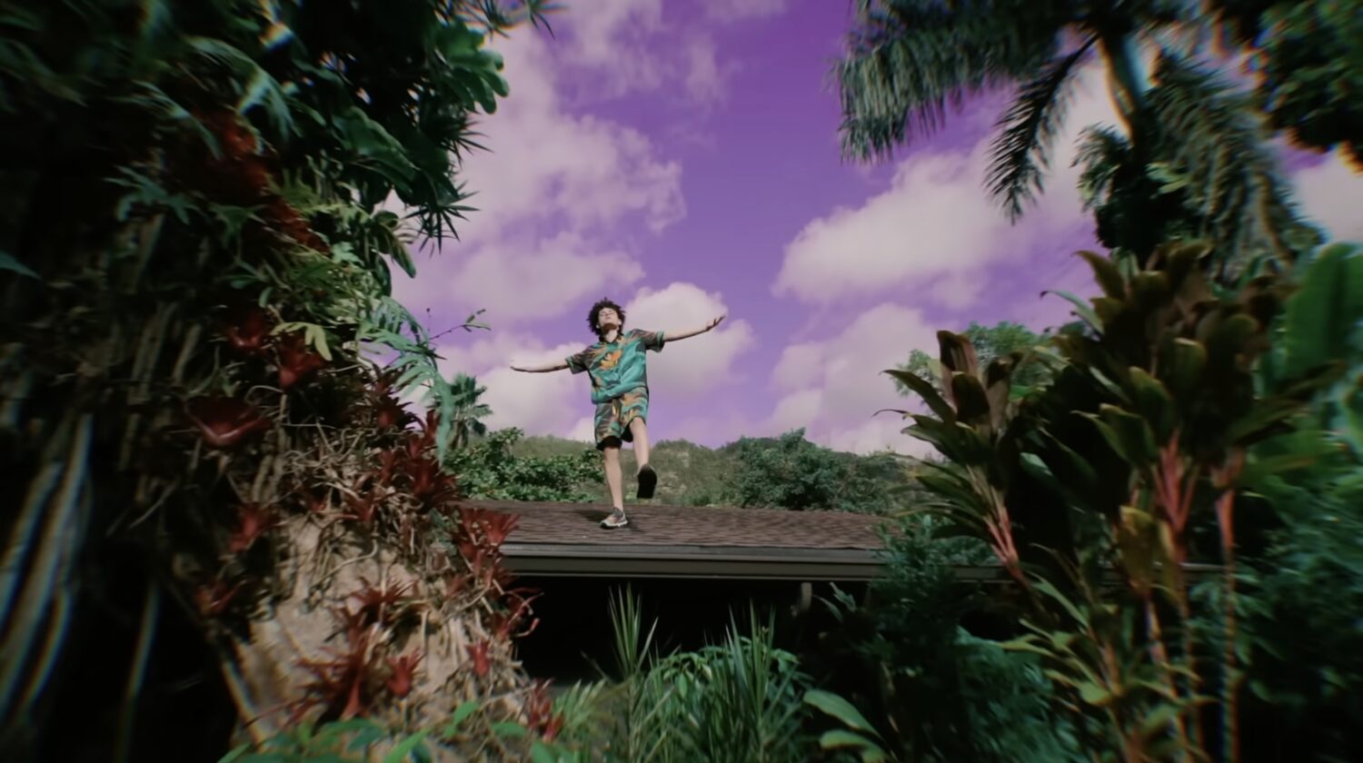 Artist on a rooftop against a purple sky, arms outstretched
